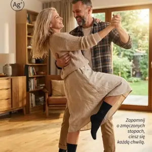Czarne skarpetki z jonami srebra DEOMED COTTON SILVER - uśmiechnięta, dojrzała para tańcząca na drewnianej podłodze, kobieta z uniesioną nogą wyraźnie eksponuje produkt na stopie - ciepłe, domowe wnętrze salonu z tekstami promocyjnymi