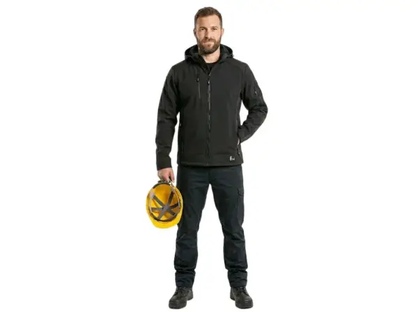 Czarna kurtka Durham softshell zaprezentowana od przodu na modelu w ciemnych spodniach roboczych, trzymającym żółty kask ochronny w prawej dłoni, z widocznym kapturem i zapiętym zamkiem, wycięte na białym tle studyjnym.