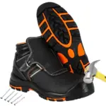 buty trekkingowe mont blanc - czarne z pomarańczowymi detalami, jeden but stoi z młotkiem uderzającym w podnosek, drugi oparty ukazuje podeszwę, obok leżą gwoździe - wycięte na białym tle studyjnym