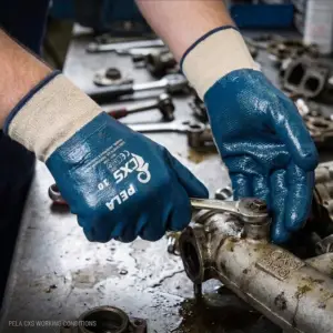 Niebieskie rękawice powlekane CXS PELA z jasnym mankietem na dłoniach mechanika trzymającego klucz płaski na zaolejonym metalowym podzespole, w tle rozmyty stół warsztatowy.
