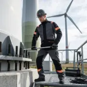 Trudnopalna bluza ochronna CXS WorkTech-Multi - szaro-czarna z pomarańczowymi detalami, ubrana przez pracownika w kasku operującego kluczem dynamometrycznym - ujęcie całej sylwetki na podeście przy turbinie wiatrowej.