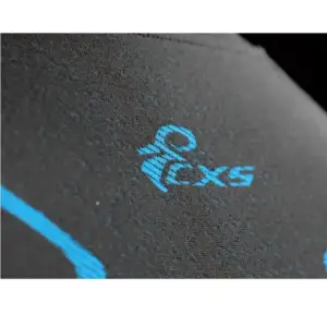 Bluzka termoaktywna SEAMFLEX - makrofotografia ciemnoszarego, teksturowanego materiału z jasnoniebieskim logo CXS - na ciemnym, rozmytym tle